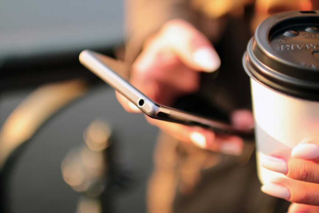 Person holding a smartphone and a takeaway coffee cup while texting outdoors.