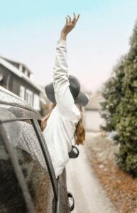 Carefree woman enjoying a rainy road trip, hand outstretched from car window.